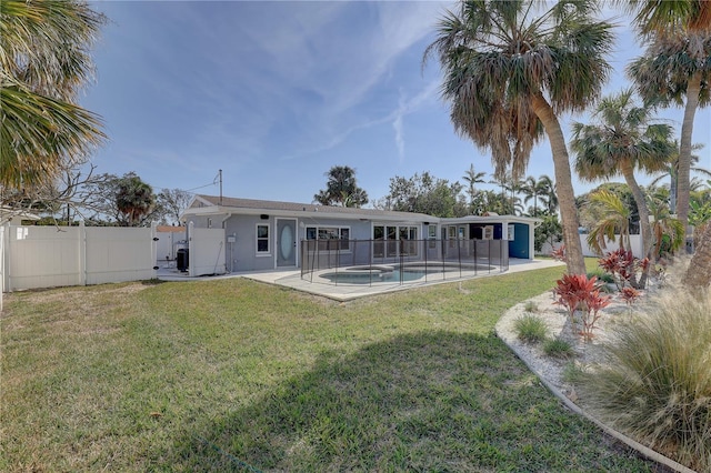 rear view of property featuring a fenced in pool, a patio area, and a lawn