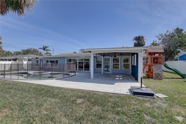 rear view of property with a playground, a yard, a fenced in pool, and a patio area