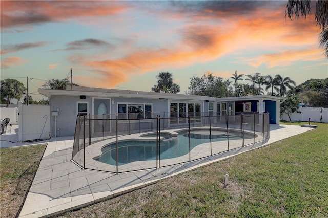 pool at dusk featuring an in ground hot tub, a yard, and a patio area