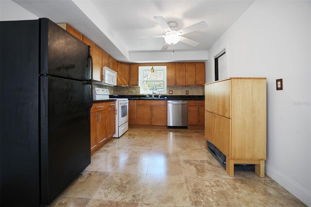 kitchen with white appliances, brown cabinetry, dark countertops, and a sink