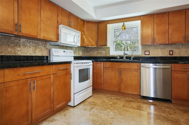 kitchen featuring brown cabinets, tasteful backsplash, a sink, dark stone countertops, and white appliances