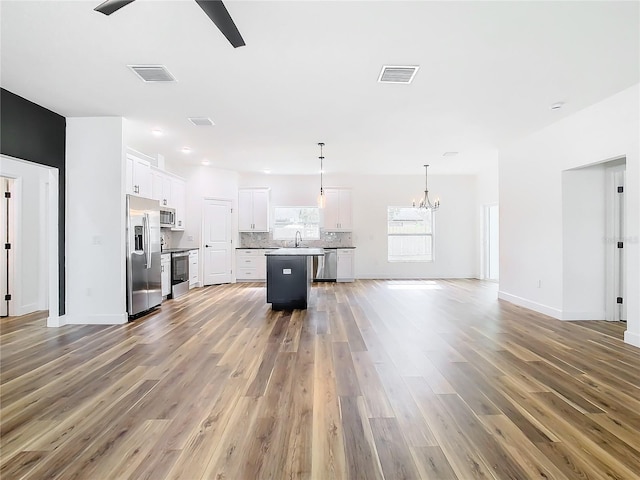 kitchen featuring appliances with stainless steel finishes, decorative light fixtures, tasteful backsplash, white cabinetry, and a center island