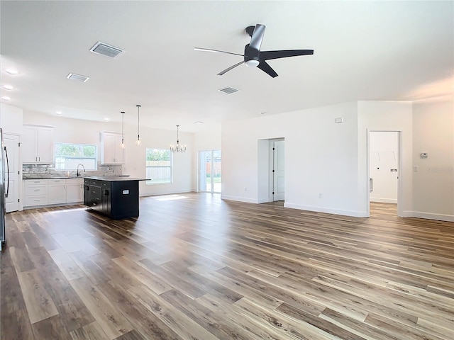 unfurnished living room with wood-type flooring, sink, and ceiling fan with notable chandelier