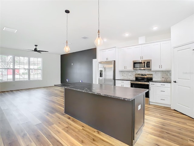 kitchen featuring appliances with stainless steel finishes, white cabinetry, a center island, decorative backsplash, and decorative light fixtures