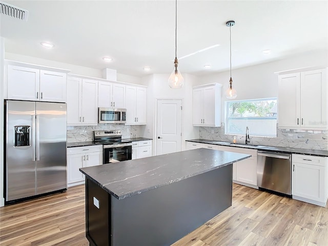 kitchen featuring white cabinetry, hanging light fixtures, stainless steel appliances, a center island, and light hardwood / wood-style floors