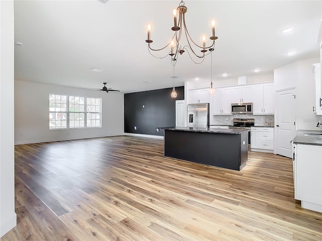 kitchen with appliances with stainless steel finishes, white cabinets, backsplash, hanging light fixtures, and a kitchen island with sink