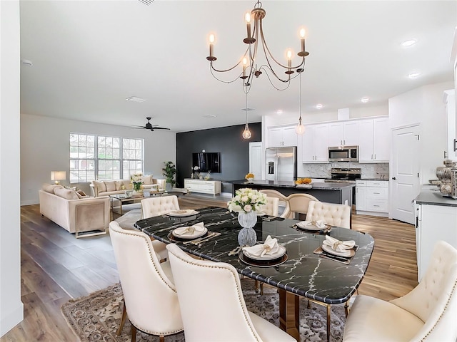 dining area with ceiling fan with notable chandelier and light hardwood / wood-style floors