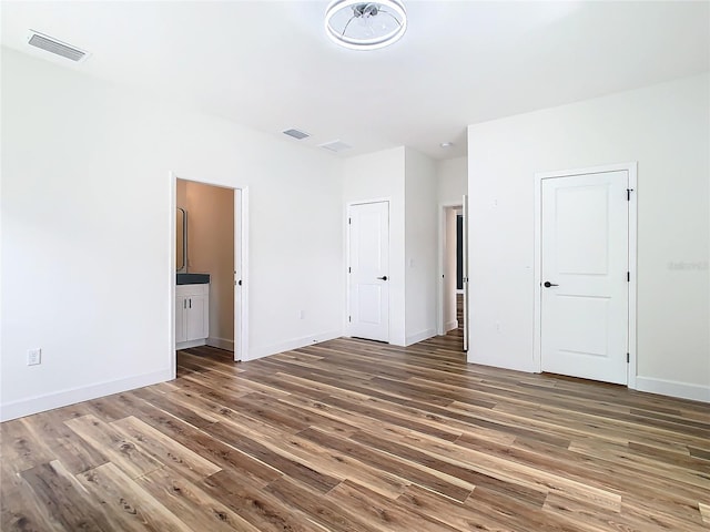 unfurnished bedroom featuring ensuite bath, dark wood-type flooring, and two closets