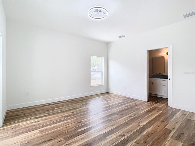 unfurnished bedroom with connected bathroom and wood-type flooring