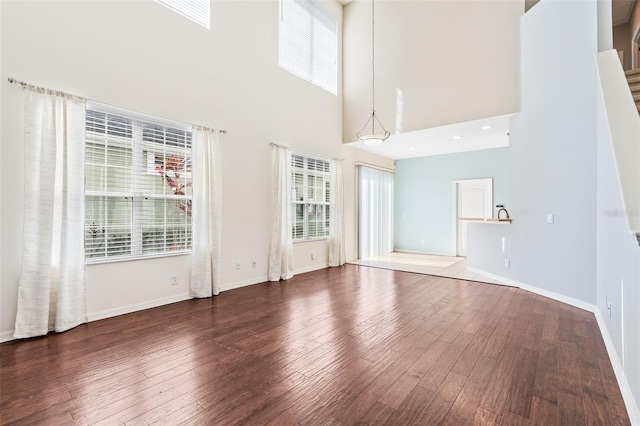 unfurnished living room featuring dark wood-type flooring, a towering ceiling, and a healthy amount of sunlight