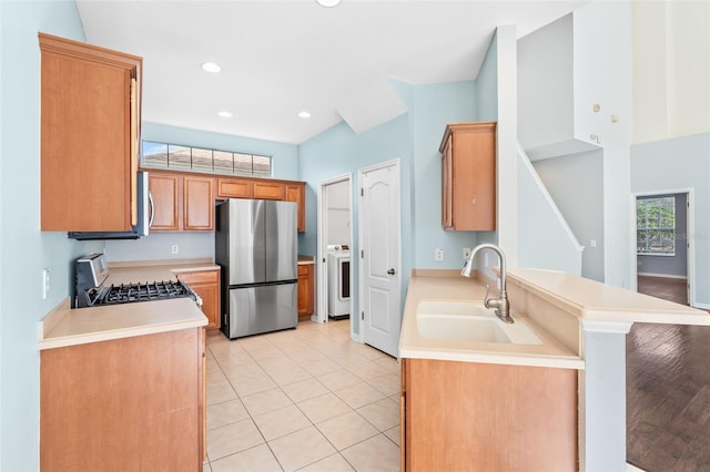 kitchen featuring sink, light tile patterned floors, appliances with stainless steel finishes, washer / clothes dryer, and kitchen peninsula