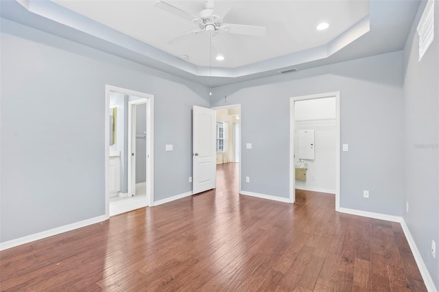 unfurnished bedroom featuring hardwood / wood-style flooring, ensuite bath, and a tray ceiling