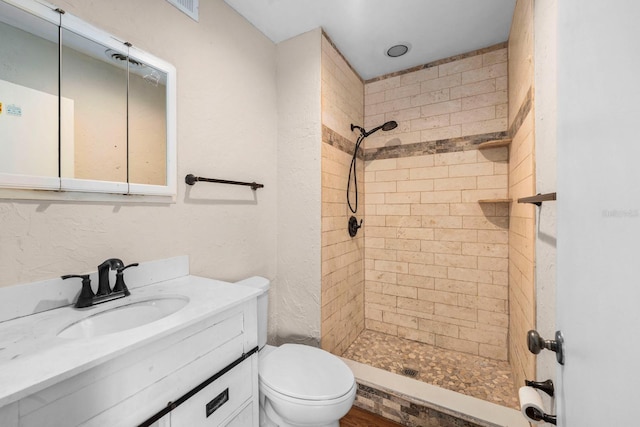 bathroom featuring a tile shower, vanity, and toilet