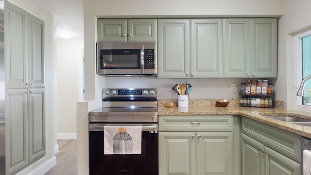 kitchen with sink, light stone counters, green cabinetry, stainless steel appliances, and light hardwood / wood-style floors