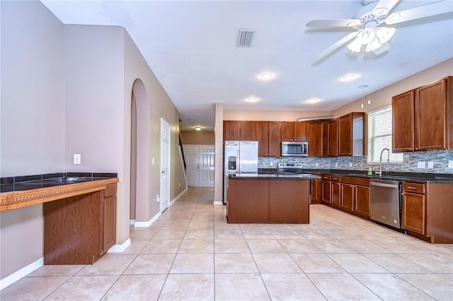 kitchen featuring light tile patterned flooring, stainless steel appliances, a kitchen island, and backsplash