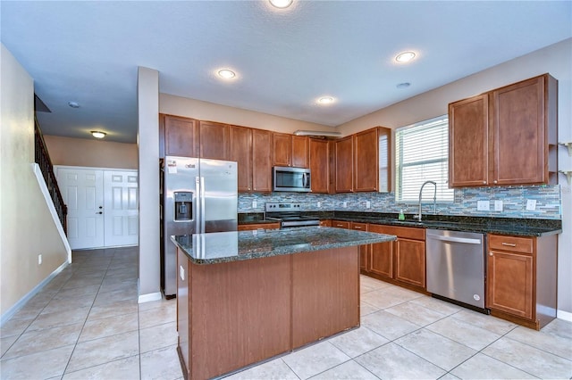 kitchen with light tile patterned floors, dark stone counters, a kitchen island, stainless steel appliances, and decorative backsplash