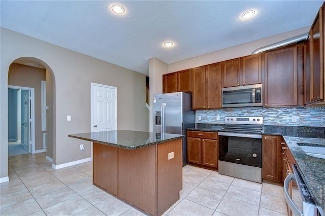 kitchen with stainless steel appliances, dark stone countertops, light tile patterned floors, and backsplash