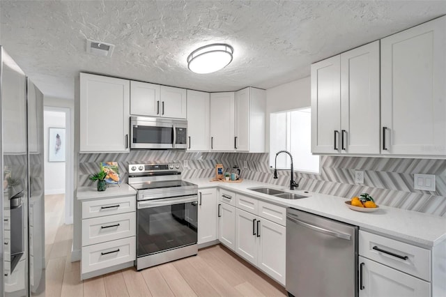 kitchen with sink, light hardwood / wood-style flooring, appliances with stainless steel finishes, tasteful backsplash, and white cabinets