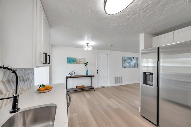 kitchen featuring sink, a textured ceiling, stainless steel fridge, light hardwood / wood-style floors, and white cabinets