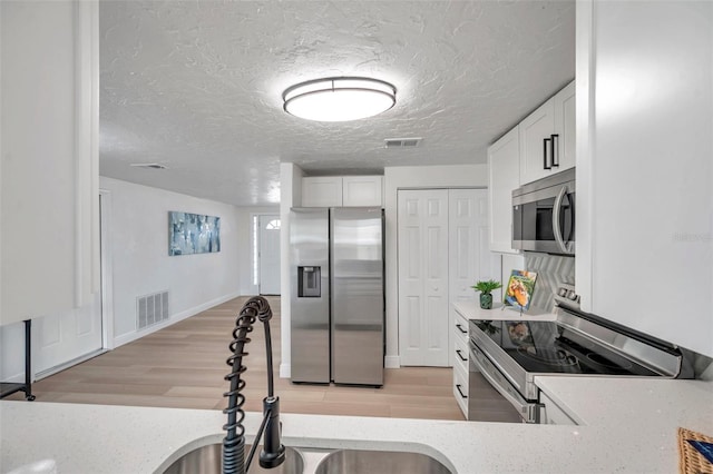 kitchen featuring white cabinetry, stainless steel appliances, sink, and light wood-type flooring