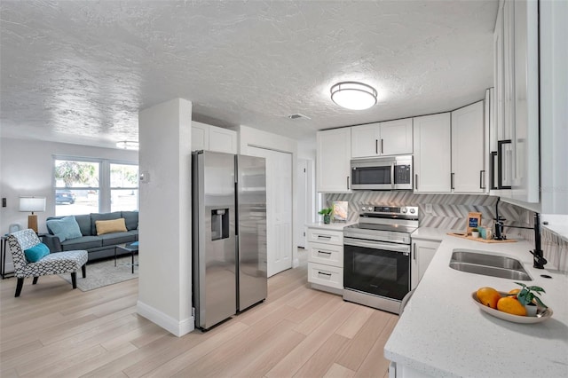 kitchen featuring white cabinetry, sink, stainless steel appliances, and light wood-type flooring