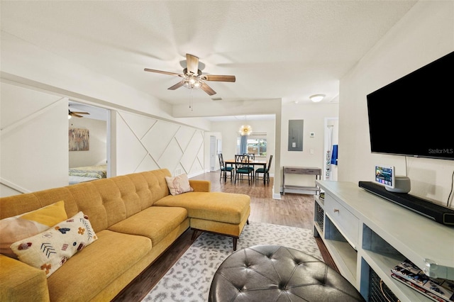 living room with electric panel, baseboards, a textured ceiling, light wood-type flooring, and ceiling fan with notable chandelier