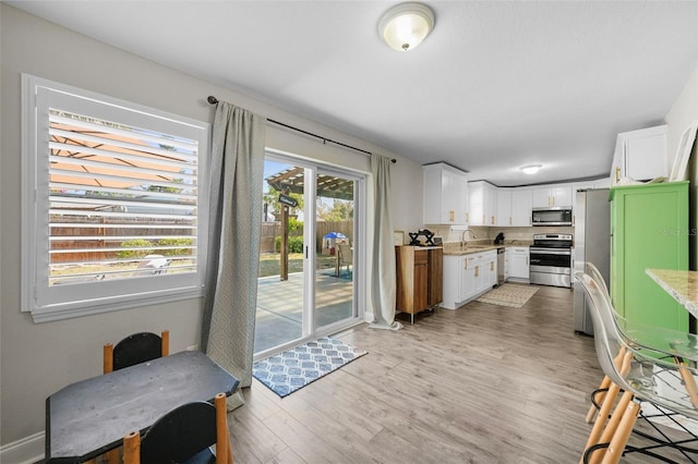 kitchen with light stone counters, light wood-style flooring, a sink, white cabinets, and appliances with stainless steel finishes