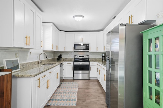 kitchen with appliances with stainless steel finishes, white cabinetry, a sink, and tasteful backsplash