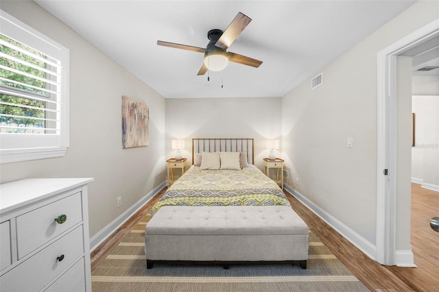 bedroom featuring a ceiling fan, wood finished floors, visible vents, and baseboards