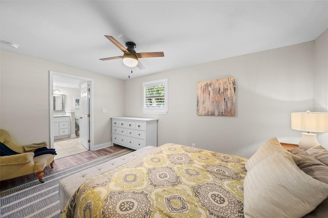 bedroom with ensuite bathroom, ceiling fan, baseboards, and light wood-style floors