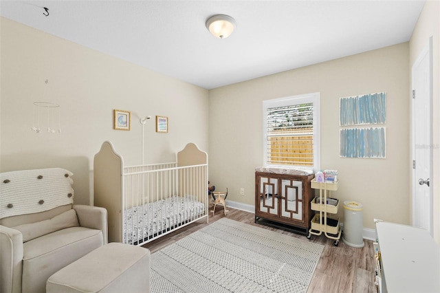 bedroom with a nursery area, light wood-type flooring, and baseboards