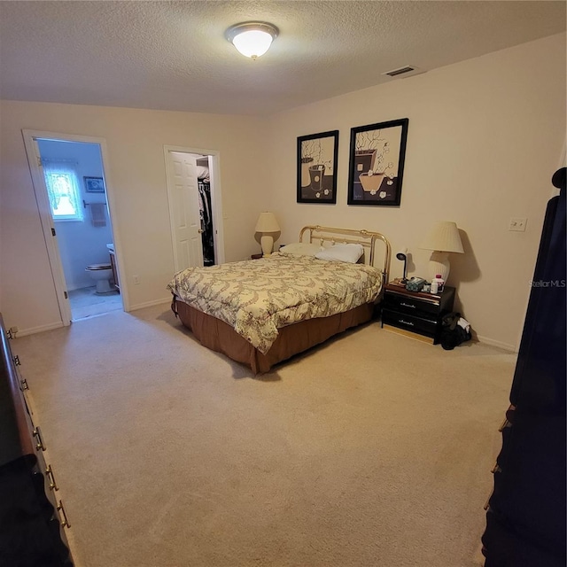 carpeted bedroom featuring ensuite bath, a spacious closet, and a textured ceiling