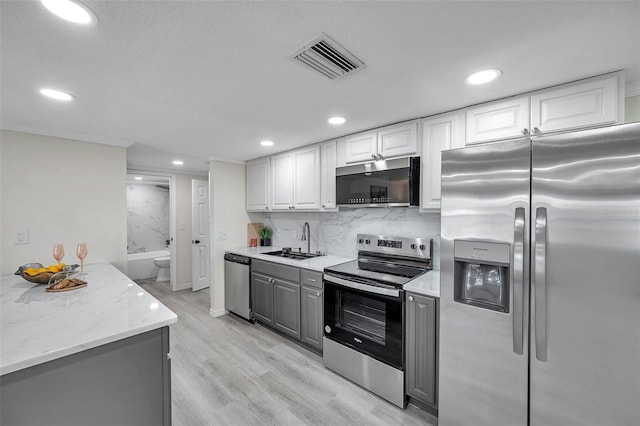 kitchen with gray cabinets, appliances with stainless steel finishes, tasteful backsplash, sink, and white cabinets