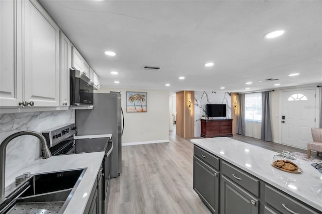 kitchen with white cabinetry, stainless steel appliances, light stone countertops, and sink