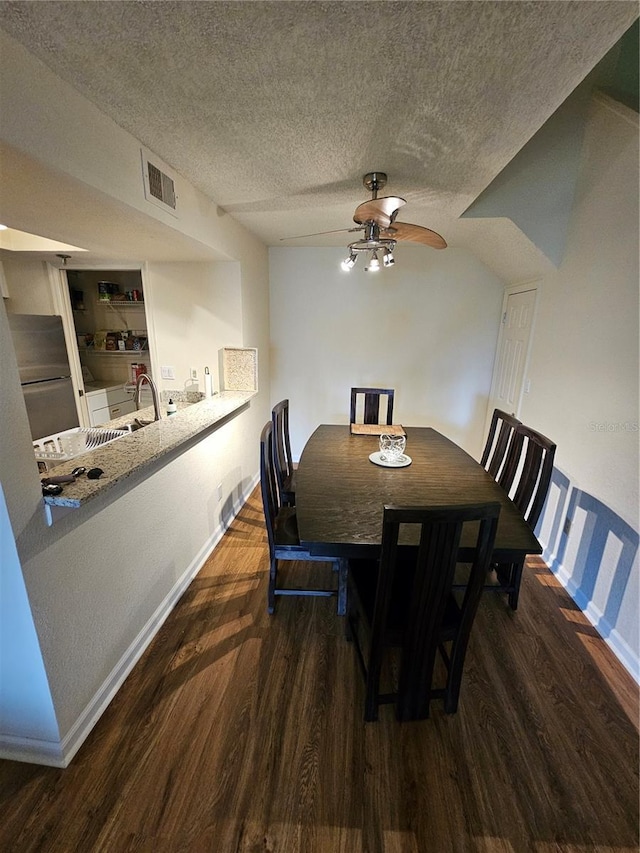 dining space featuring ceiling fan, dark wood-type flooring, sink, and a textured ceiling