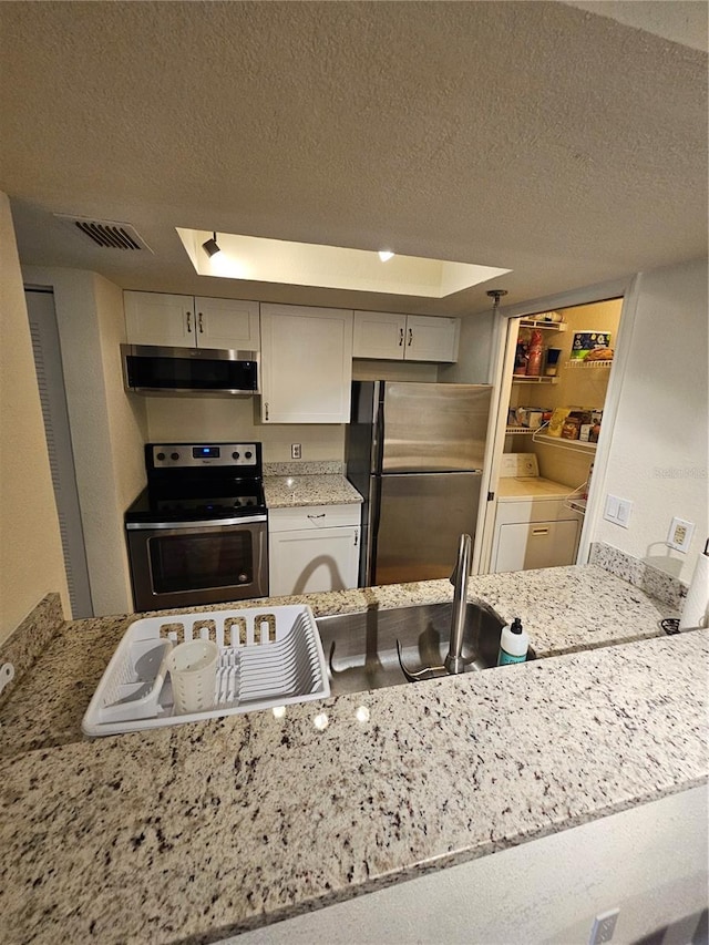 kitchen featuring stainless steel appliances, light stone countertops, a textured ceiling, and ventilation hood