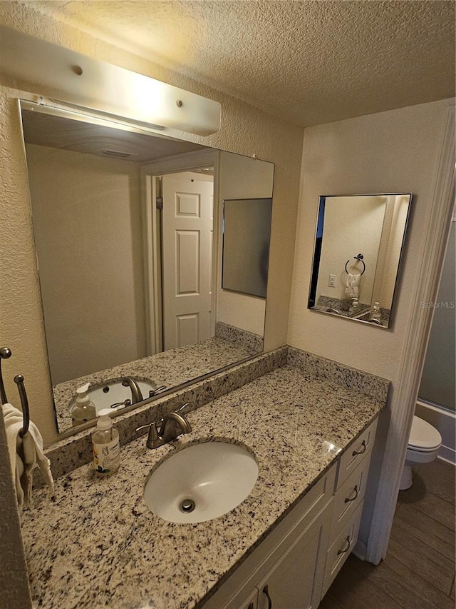 bathroom featuring vanity, hardwood / wood-style floors, toilet, and a textured ceiling