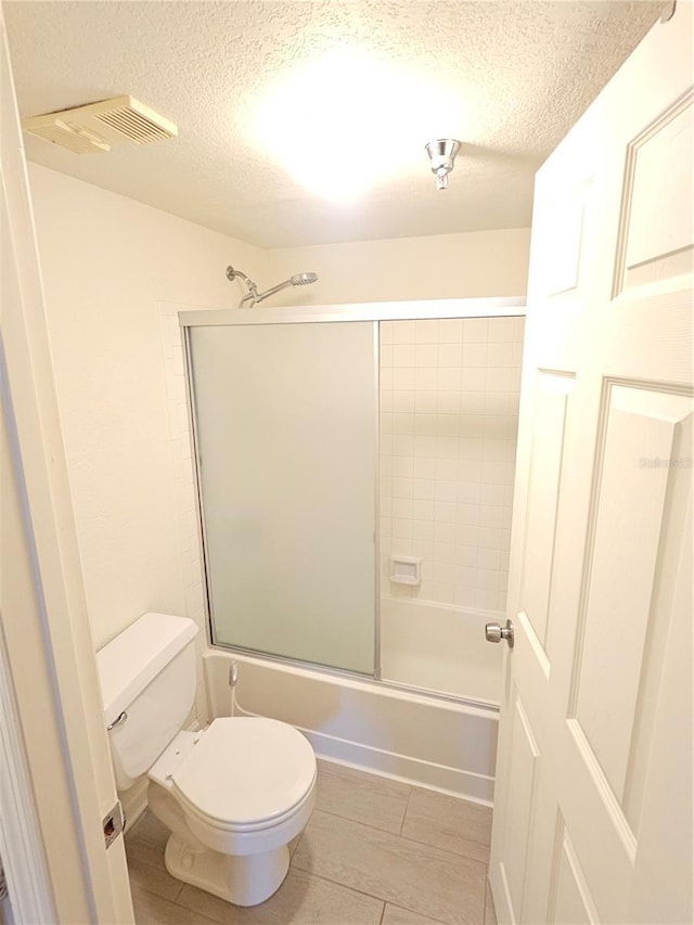 bathroom with combined bath / shower with glass door, a textured ceiling, and toilet