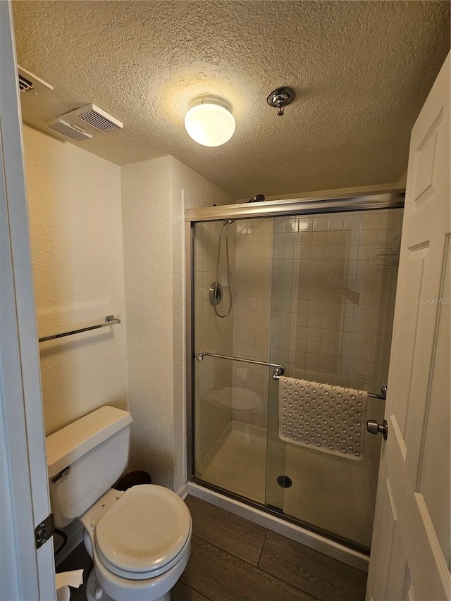 bathroom featuring a textured ceiling, a shower with door, and toilet