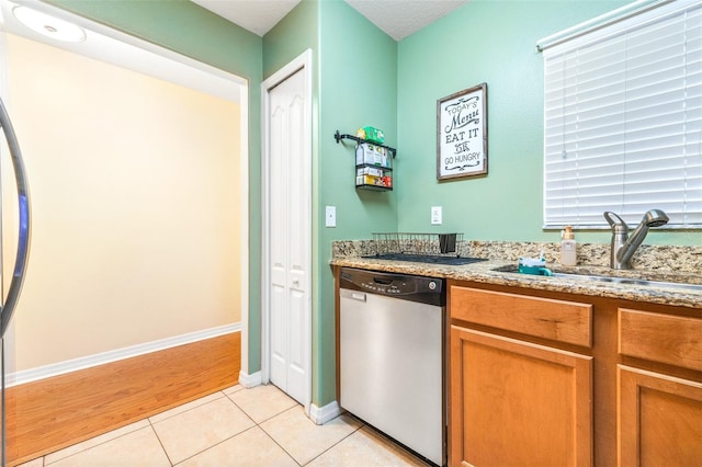 kitchen with light stone countertops, sink, stainless steel dishwasher, and light tile patterned floors