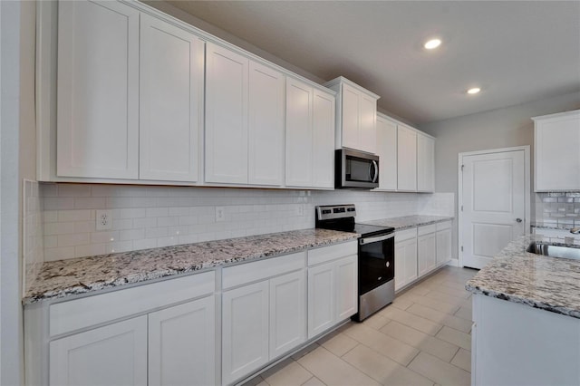 kitchen featuring sink, light stone counters, appliances with stainless steel finishes, decorative backsplash, and white cabinets