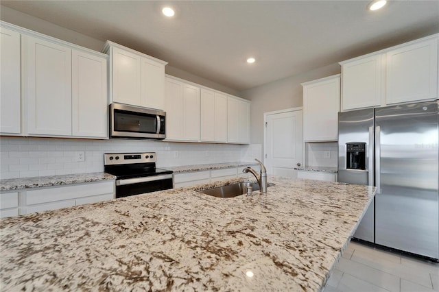 kitchen with appliances with stainless steel finishes, tasteful backsplash, sink, white cabinets, and light stone counters