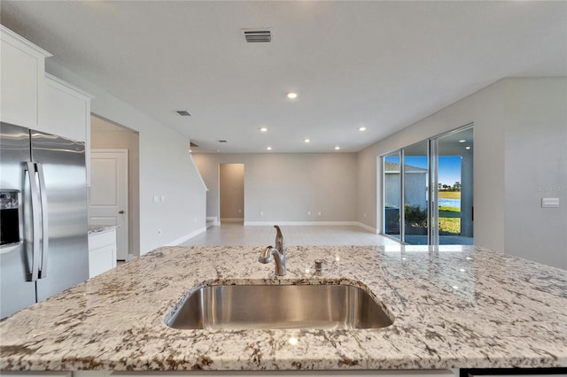 kitchen featuring light stone counters, sink, a kitchen island with sink, and stainless steel fridge