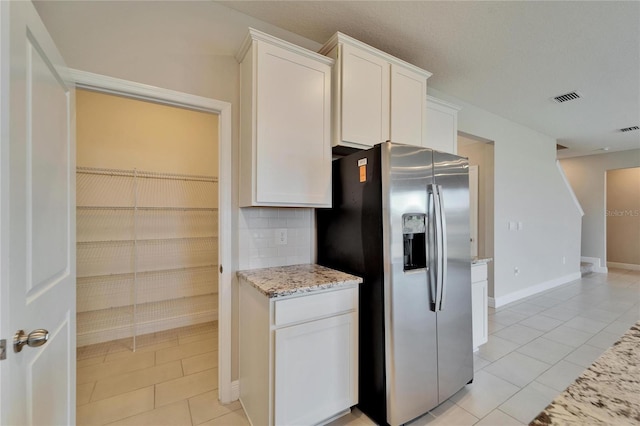 kitchen with light tile patterned floors, stainless steel refrigerator with ice dispenser, tasteful backsplash, light stone counters, and white cabinets