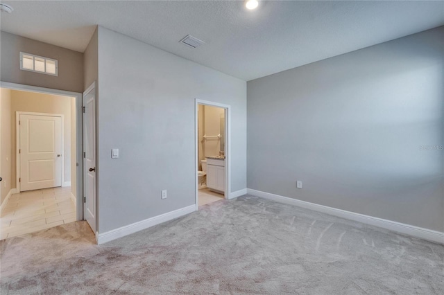 unfurnished bedroom featuring light carpet, a textured ceiling, and ensuite bathroom