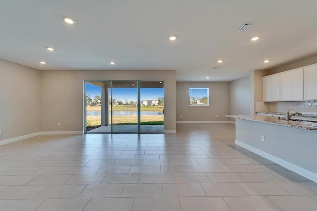 kitchen featuring sink, white cabinetry, a water view, light stone counters, and tasteful backsplash