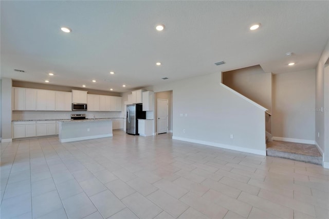 kitchen with stainless steel appliances, white cabinets, and a center island with sink