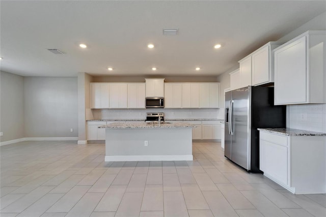 kitchen with stainless steel appliances, a kitchen island with sink, white cabinets, and light stone counters