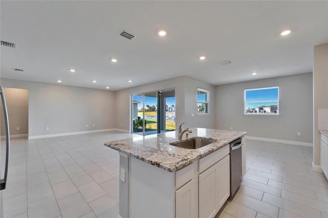 kitchen featuring sink, dishwasher, white cabinetry, light stone countertops, and a center island with sink