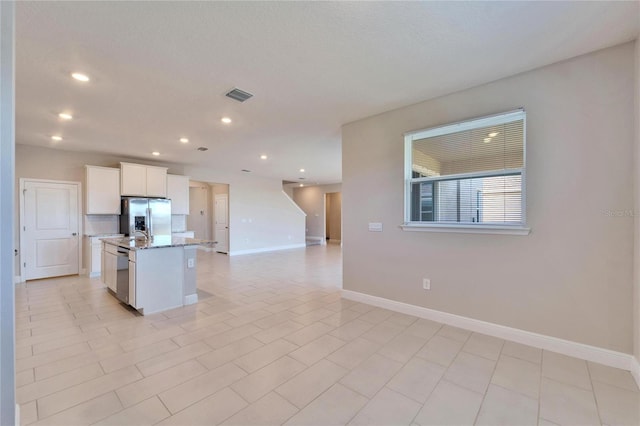 kitchen with light stone counters, a textured ceiling, appliances with stainless steel finishes, a kitchen island with sink, and white cabinets